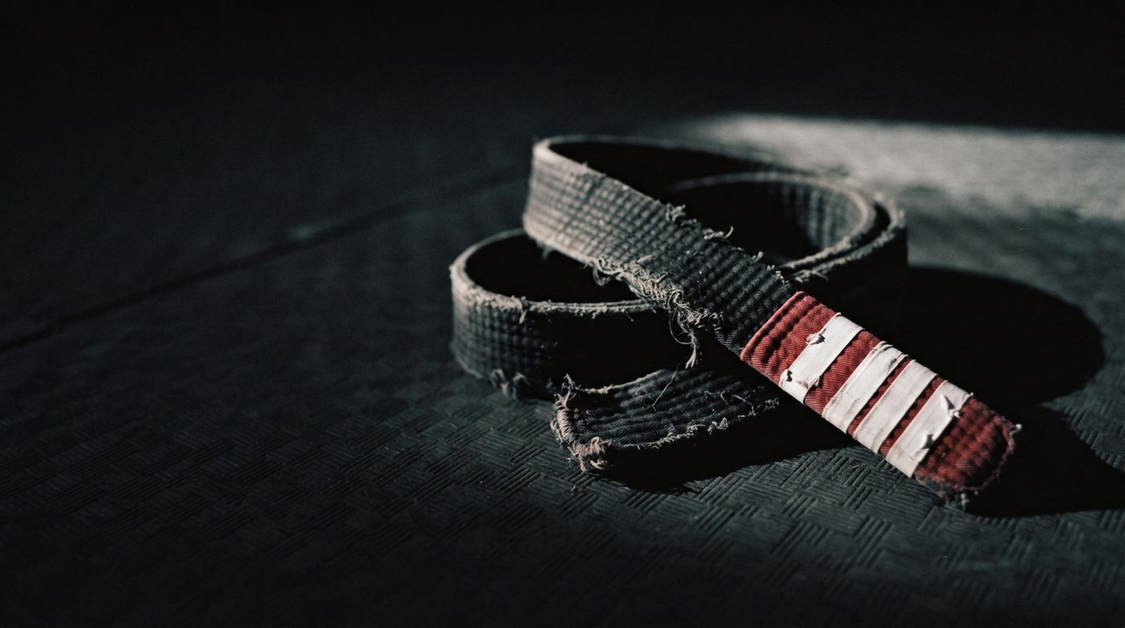 Faixa preta de jiu-jitsu gasta, com ponteira vermelha, sobre o tatame